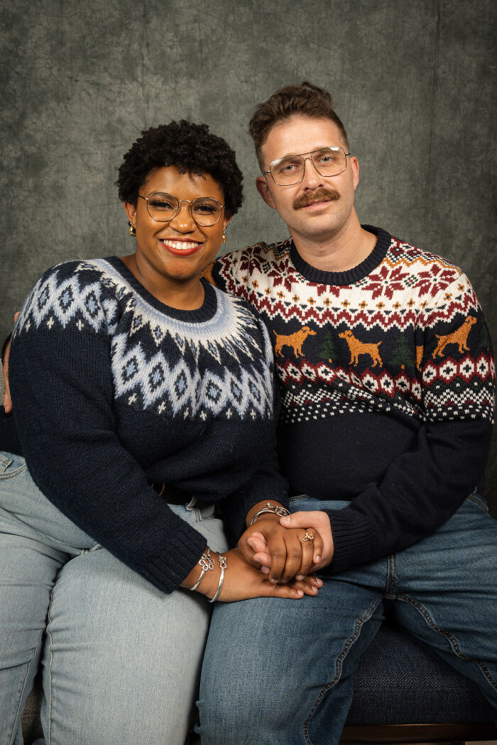 Couple posing in 80s-style outfits for an anniversary photoshoot, wearing matching patterned sweaters and jeans.