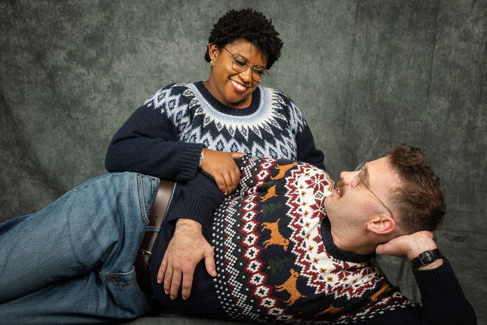 Couple in 80s sweaters, smiling and posing for an anniversary photoshoot with a retro vibe.