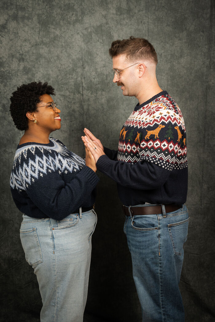 Couple in 80s-themed photoshoot wearing matching patterned sweaters, gazing at each other in a retro setting.