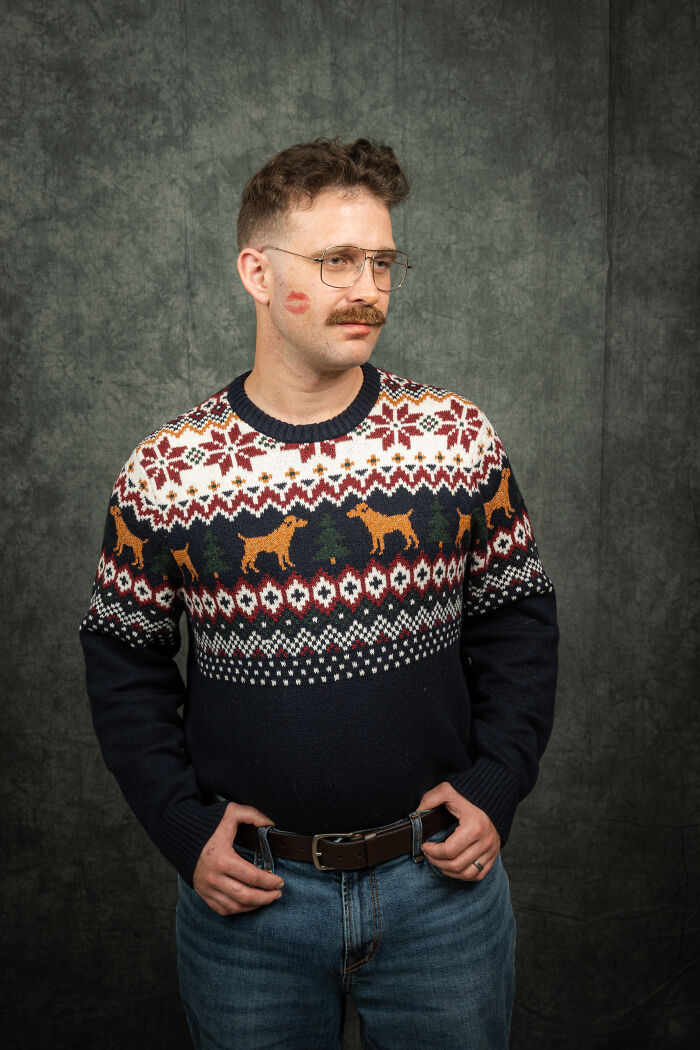 Man with glasses in 80's style sweater, mustache, and kiss mark on cheek in anniversary photoshoot.