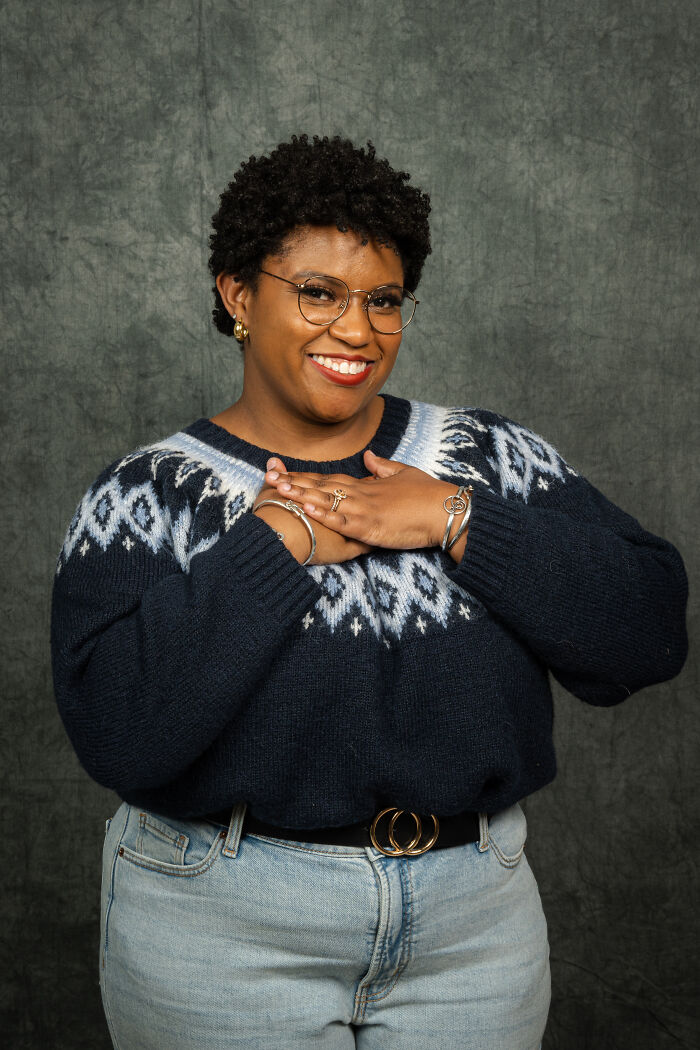 Person wearing glasses and a retro sweater, smiling indoors, highlighting an 80's photoshoot vibe for an anniversary.