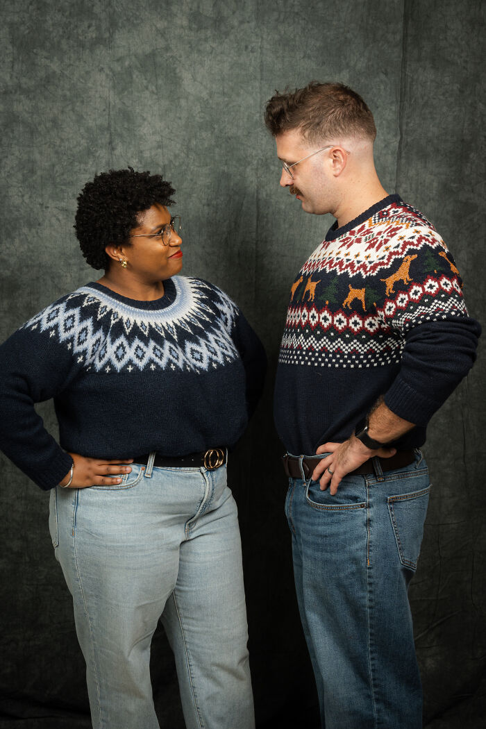 Couple in 80s fashion posing for anniversary photoshoot, wearing matching patterned sweaters.