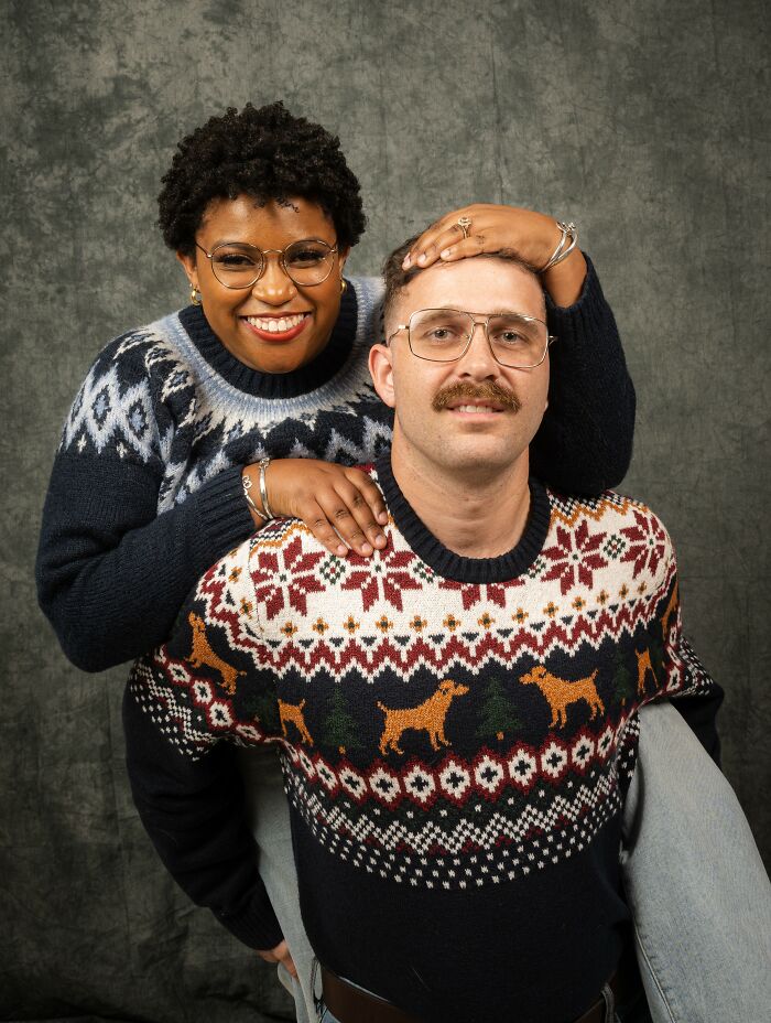 Couple posing in awkward 80s photoshoot with matching patterned sweaters and smiling expressions.