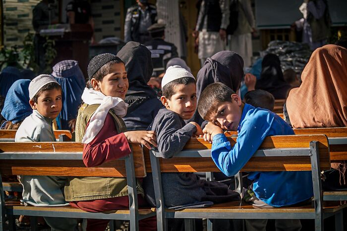 Afghan children wearing traditional clothing sitting on benches outdoors while traveling in Afghanistan.