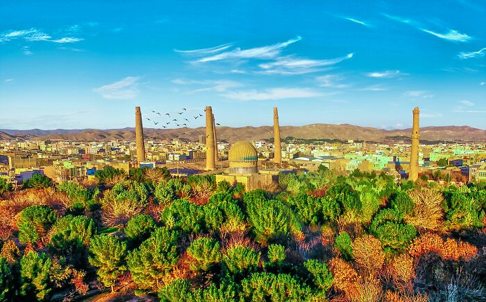 Afghanistan cityscape with historic minarets and lush greenery under a bright blue sky during travel photography.