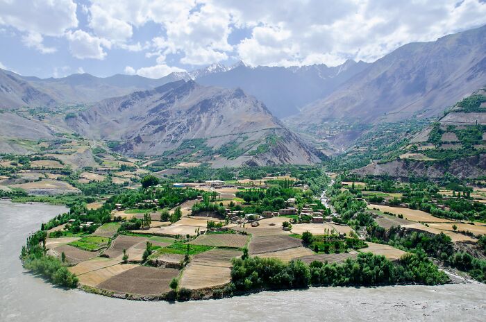 Lush green farmland and a river surrounded by mountains while traveling in Afghanistan, showcasing scenic countryside views.