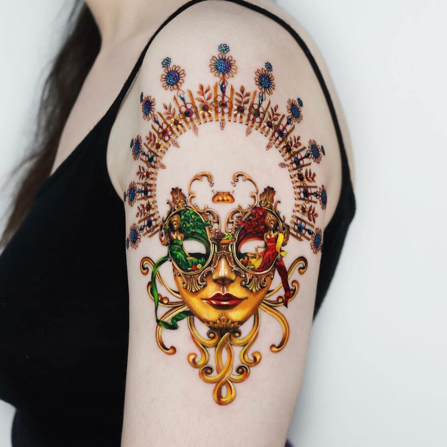 Golden tattoo featuring an intricate mask design on a person's upper arm, showcasing precision by a Manhattan-based artist.