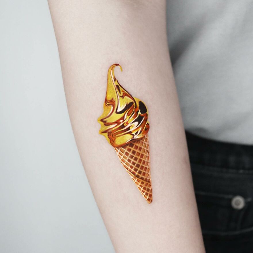 Golden tattoo of an ice cream cone on an arm, crafted by a Manhattan-based artist.