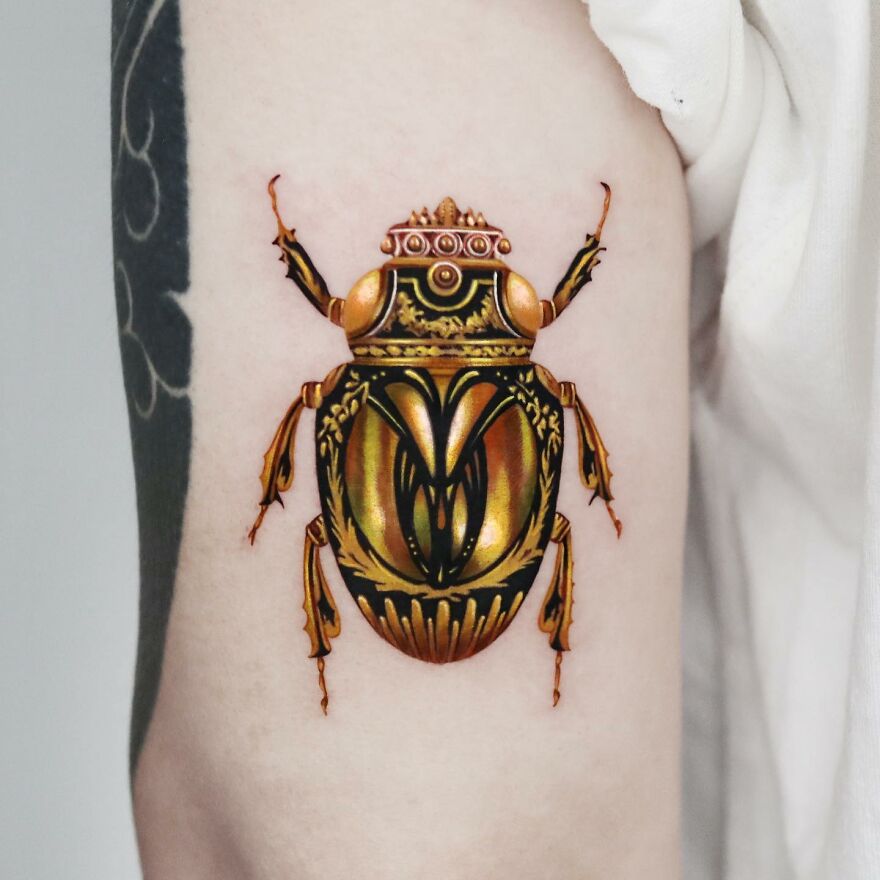 Golden beetle tattoo on arm, created with precision by Manhattan-based artist.