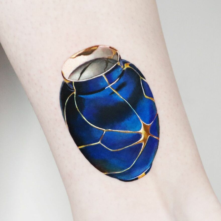 Golden tattoo in 3D style featuring a blue c*****d vase design by Manhattan-based artist, displayed on skin.