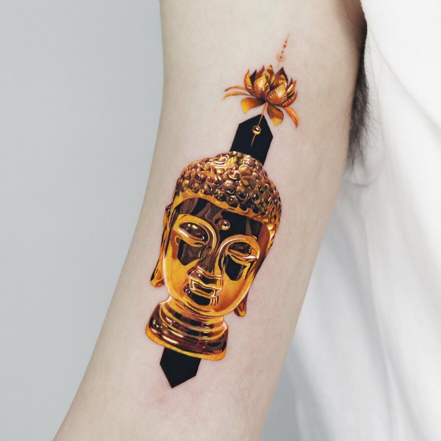Golden tattoo of Buddha's head with a lotus flower, crafted by a Manhattan-based artist.
