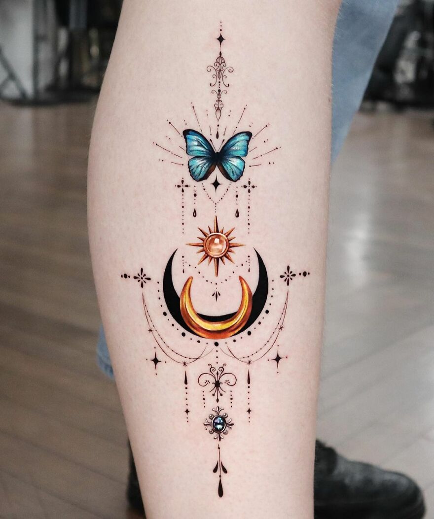 A golden tattoo with a crescent moon, sun, butterfly design by a Manhattan-based artist.
