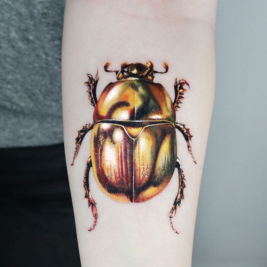 Golden beetle tattoo on forearm, crafted with precision by Manhattan-based artist.