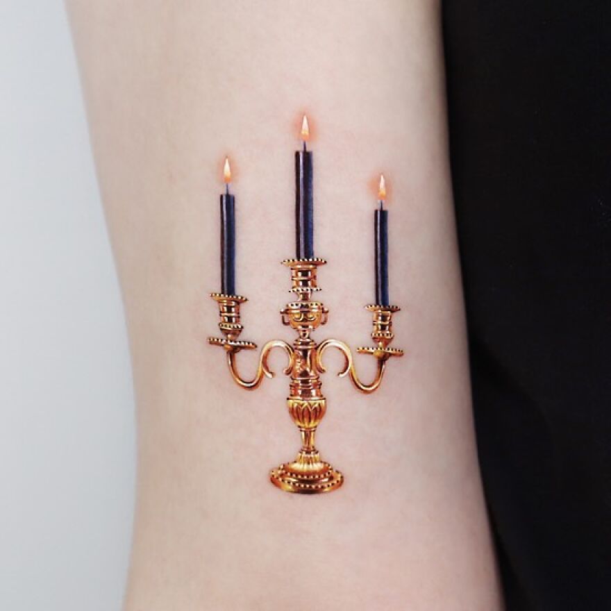 Golden tattoo of a detailed candelabra on skin, created by a Manhattan-based tattoo artist.