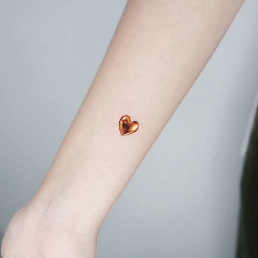Golden heart tattoo on arm by Manhattan-based artist, showcasing precision and dazzling design.
