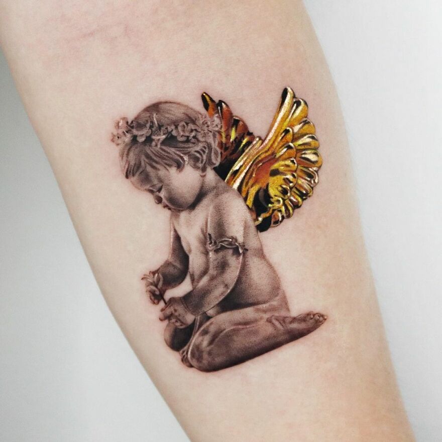 Golden tattoo of a cherub with intricate wings by Manhattan-based artist, showcasing precision and artistry.