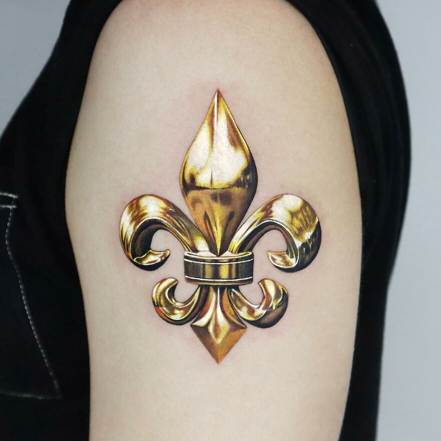 Golden fleur-de-lis tattoo on arm, showcasing precision by Manhattan-based artist.