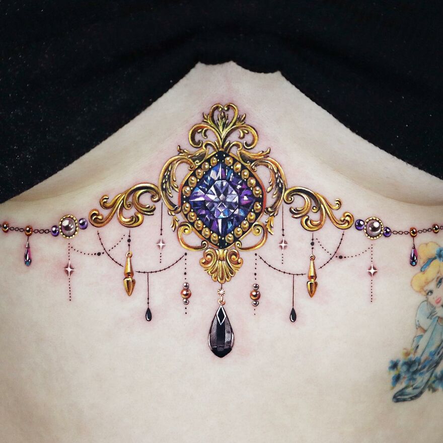 Ornate golden tattoo on skin, featuring intricate jewel and scroll designs by Manhattan-based tattoo artist.