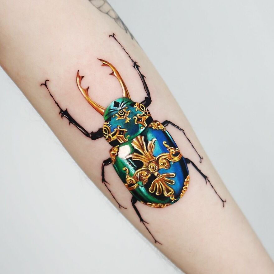 Golden tattoo of an ornate beetle design on an arm, crafted by a Manhattan-based artist.