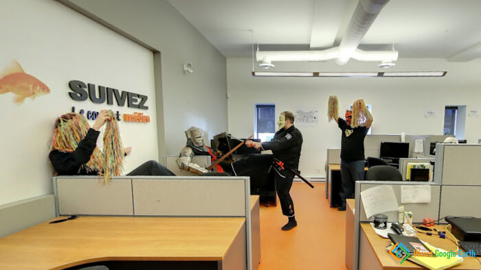 Office workers in costumes having a playful and amusing moment captured by Google Maps inside a modern workspace.