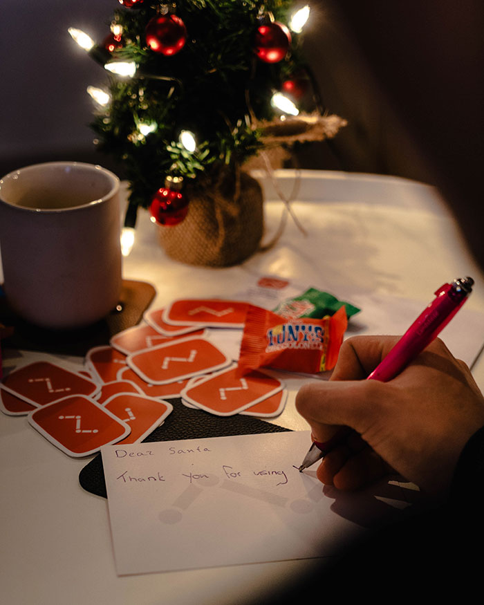 Person writing a letter near small Christmas tree