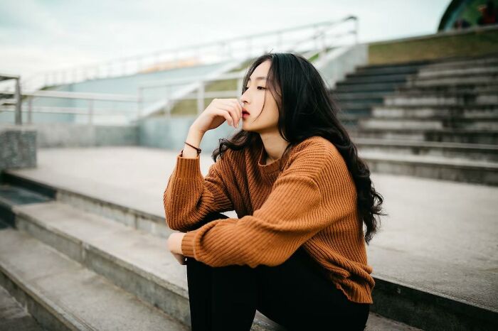 Young woman sitting on outdoor steps, deep in thought, illustrating things everyone does but pretend not to.