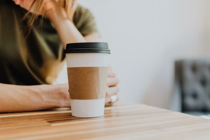 Person sitting at table with disposable coffee cup, illustrating things everyone does but pretend not to admit.