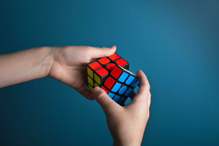 Hands solving a colorful Rubik's Cube against a plain blue background, illustrating common challenges everyone faces.