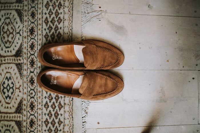 Brown suede loafers placed neatly on a patterned rug and wooden floor illustrating money-saving life hacks.