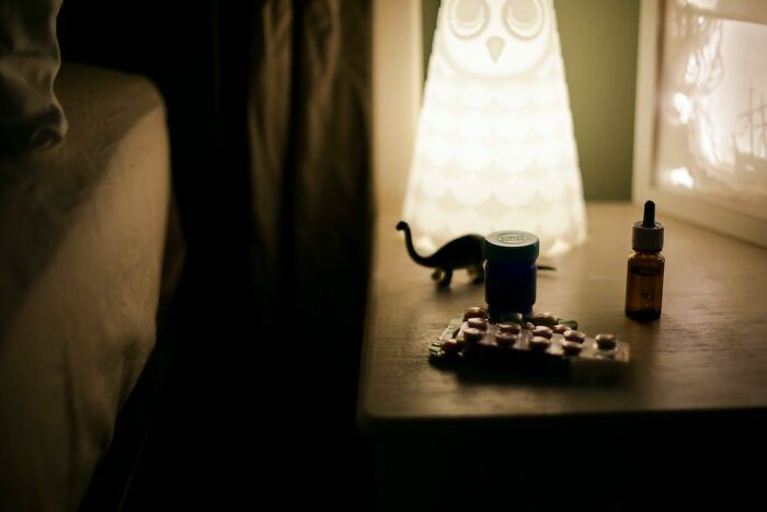 A dimly lit bedside table with medication bottles and an owl-shaped lamp, highlighting criminally overpriced items.