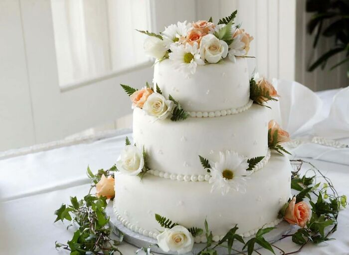Three-tier white cake decorated with flowers and greenery, example of something considered criminally overpriced.