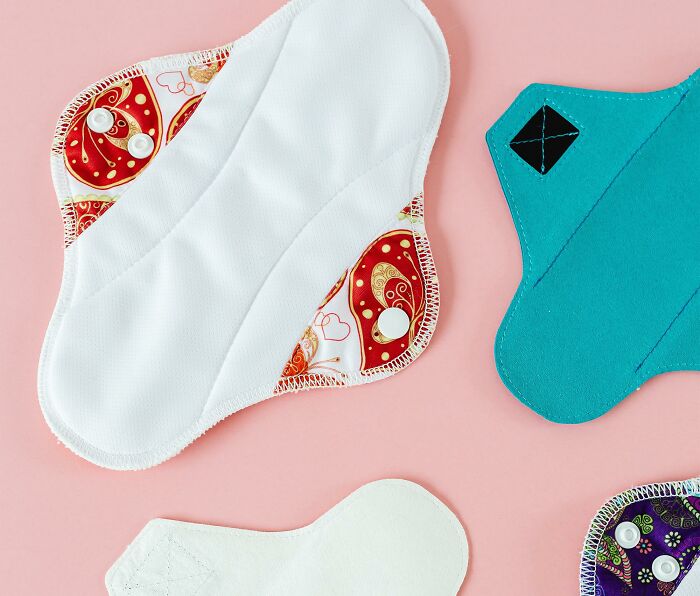 Cloth menstrual pads in various colors and patterns laid out on a pink background, highlighting criminally overpriced items.