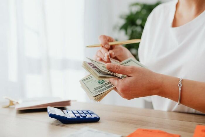 Person counting cash with a calculator on the table, illustrating money-saving life hacks in daily budgeting.