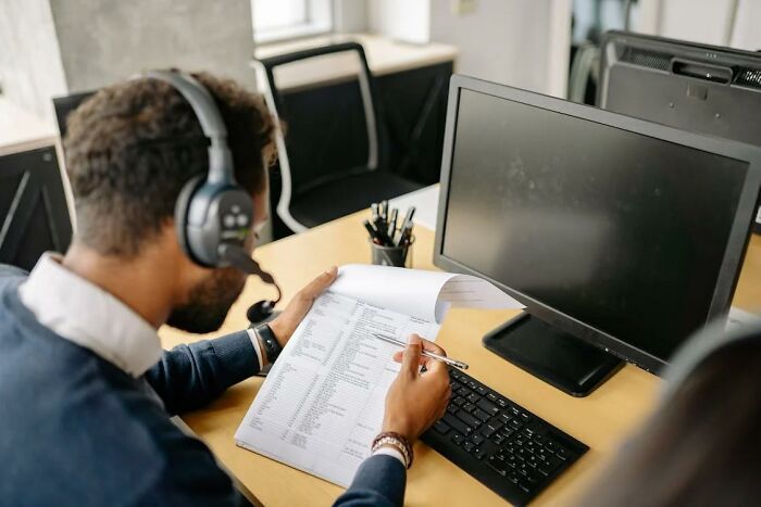 Man wearing headset and reviewing documents at his desk in an office illustrating money-saving life hacks
