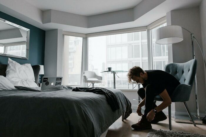 Man in modern bedroom, tying shoes by window, illustrating life-saving tips shared by private investigator.