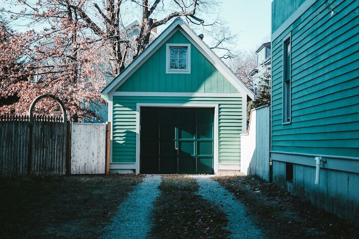 Green detached garage with a closed door at the end of a gravel driveway in a suburban setting.