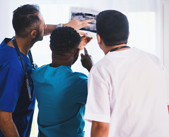 Three doctors examining an X-ray together, sharing second opinion stories in a clinical setting.