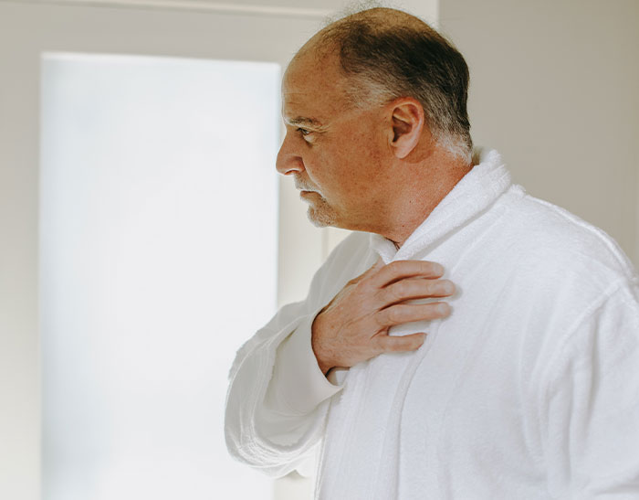 Middle-aged man in white robe holding his chest, reflecting concern in a medical second opinion context.