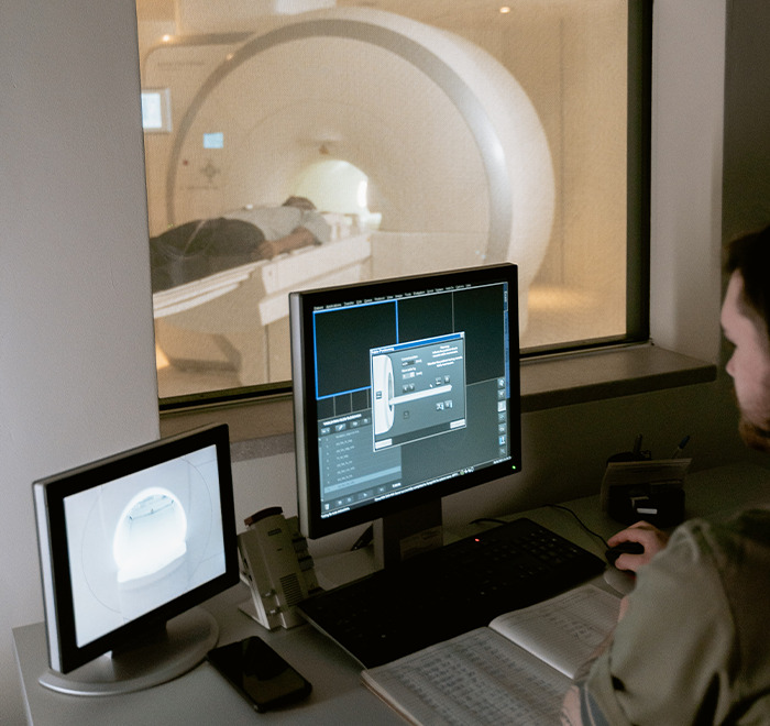 Doctor monitoring MRI scan results on computer screens while patient undergoes imaging, illustrating second opinion medical stories.