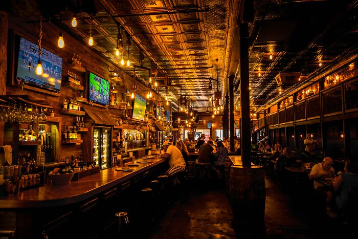 Dimly lit bar interior with people sitting alone or in groups, evoking the fear of going downstairs after lights go off.