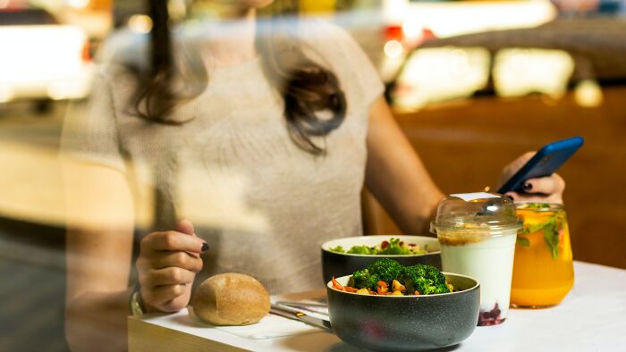 Person checking phone while eating a meal alone in a restaurant, illustrating fear of doing things alone like going downstairs after lights off.