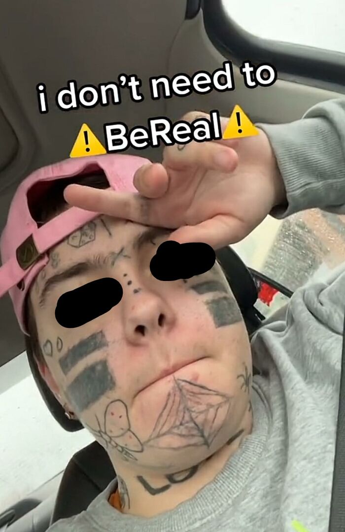 Person with humorous tattoos on their face, wearing a pink cap, in a car, embodying inkshaming fun.