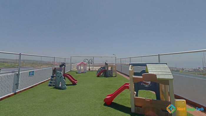 Rooftop playground with colorful slides and playhouses under clear sky, an amusing moment captured by Google Maps.