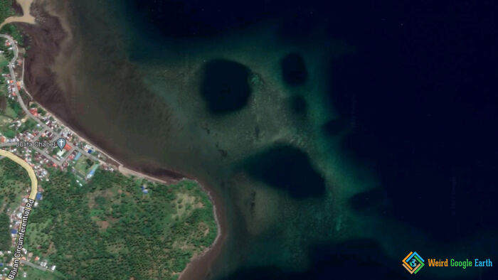 Aerial view of a coastline showing unusual dark shapes underwater, one resembling a large hand on Google Maps.
