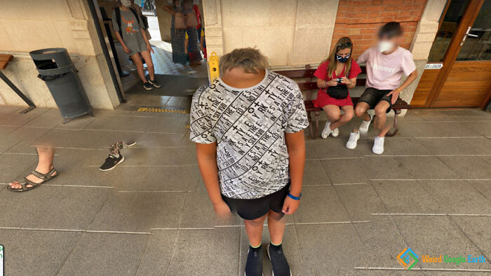 Boy with distorted head standing indoors with people sitting and walking nearby in an amusing Google Maps capture.