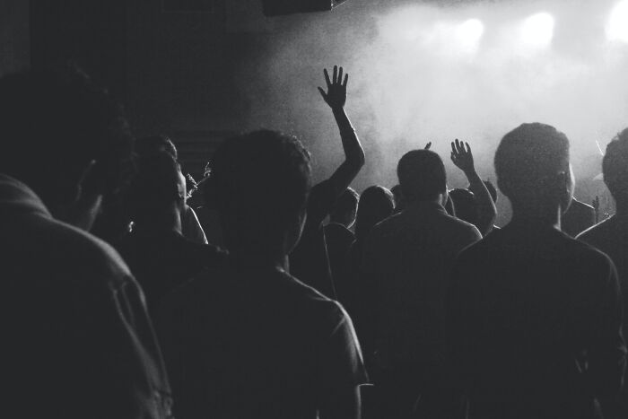 Crowd of people in a dark room with raised hands, illustrating fear and hesitation in a low-light setting.