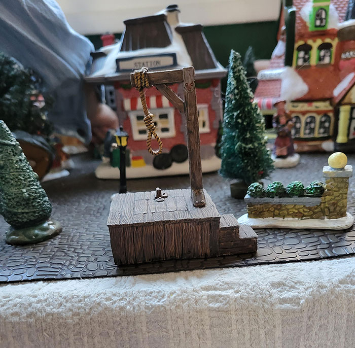 Humorous Christmas village scene with a festive miniature gallows, adding a quirky twist to holiday decor.