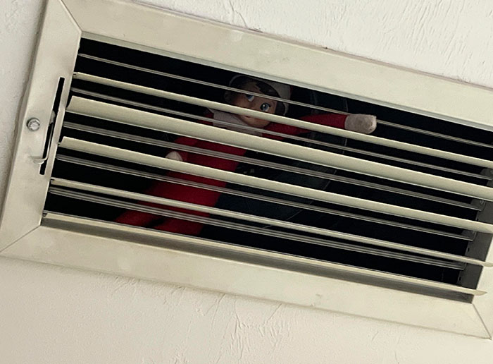 Elf doll with a sense of humor is hiding in an air vent, adding amusement to Christmas decor.