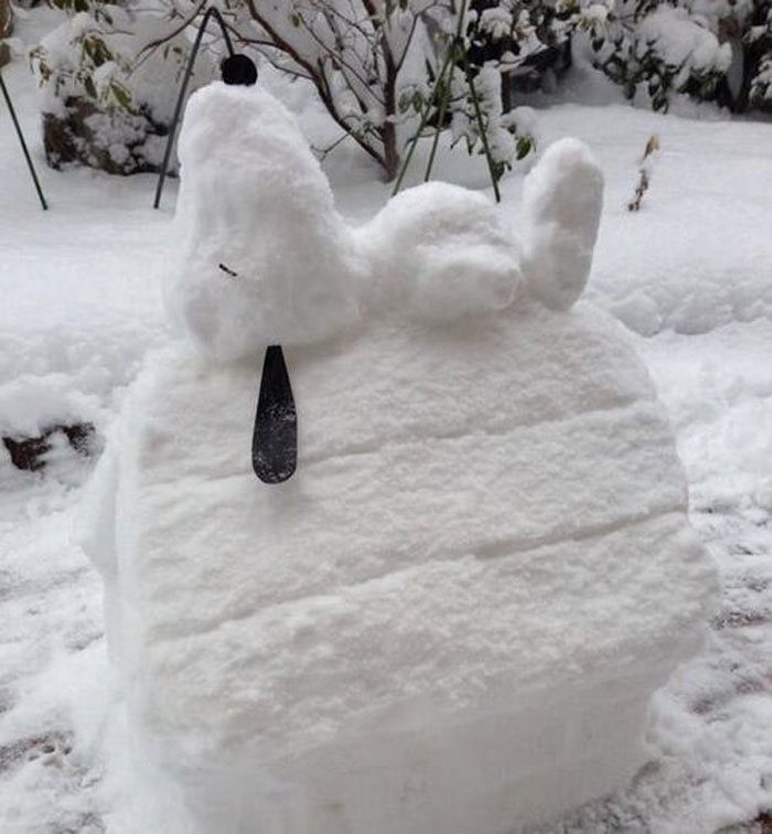 Snow sculpture of Snoopy on his doghouse in a snowy Canadian setting, showcasing creative winter art.