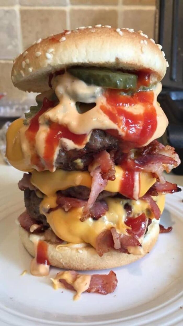 Close-up of a double bacon cheeseburger dripping with sauces and pickles, featured in a dish rating Facebook group.